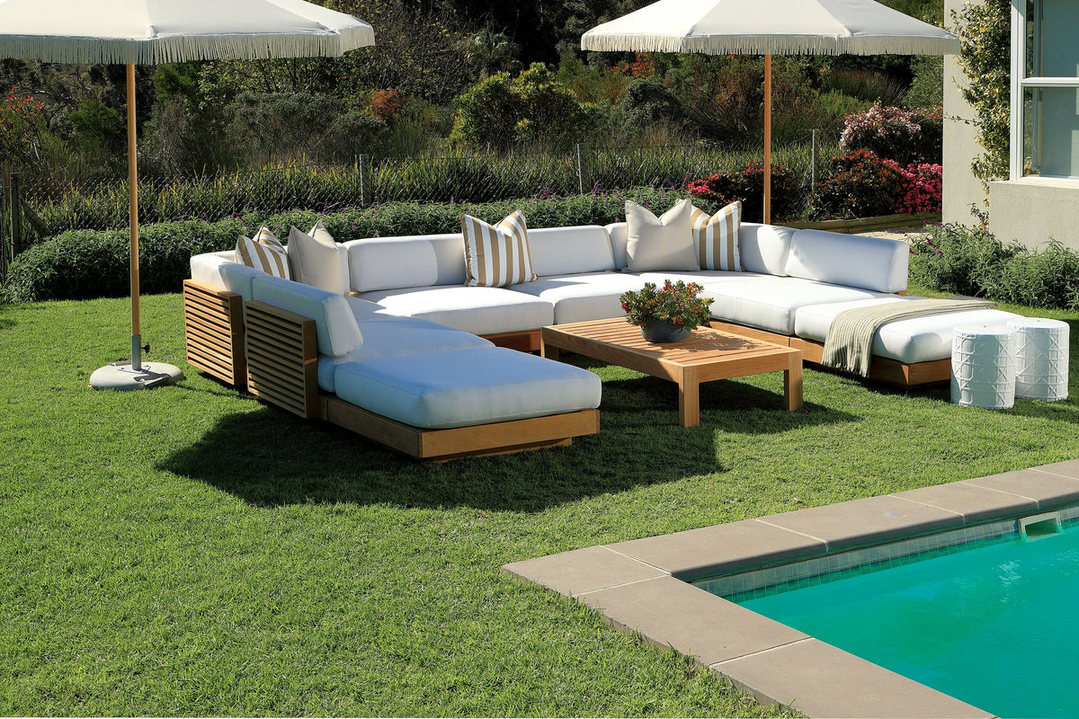 California outdoor modular sofa with ottoman and coffee table on a lawn beside a pool, under two fringed umbrellas