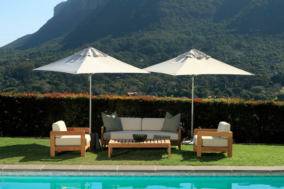 Malibu outdoor sofa, two armchairs and coffee table under white umbrellas beside a pool, with a mountain behind